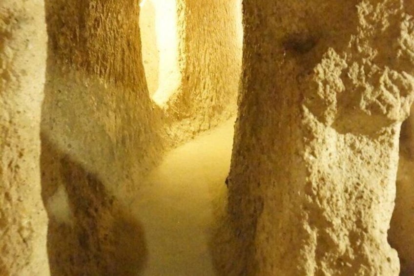 Un estrecho pasaje con paredes de piedra tosca y una fuente de luz al final. 4