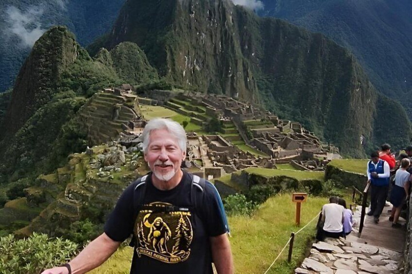 Een persoon staat voor de ruïnes van Machu Picchu, met een bergachtig landschap op de achtergrond. 3