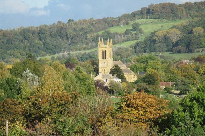 Eine Kirche mit einem hohen Turm, umgeben von Bäumen in Herbstfarben und sanften Hügeln. 4