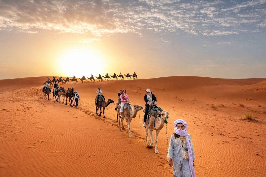 A group of people riding camels across a desert landscape during sunset. 1