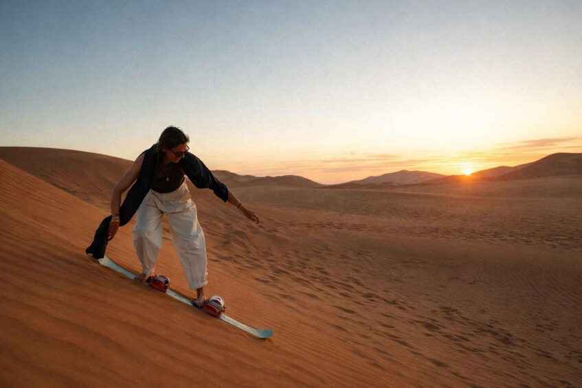 A person snowboarding down a sand dune at sunset. 4