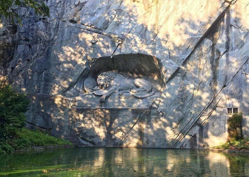 A rock formation with a carved lion statue and a small pond in front. 5