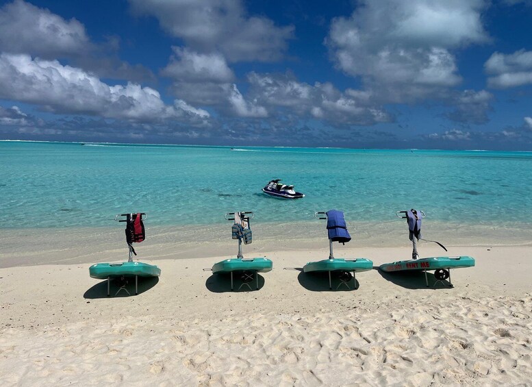 A beach with four green lounge chairs and a jet ski in the water. 1