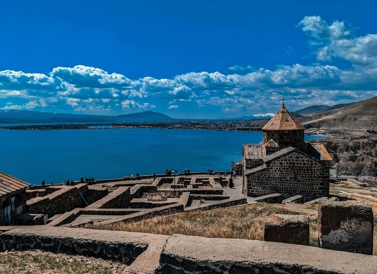 A stone church with a bell tower overlooking a lake with mountains in the distance. 1