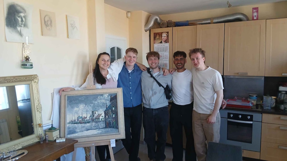 A group of people in a kitchen with a framed painting of a town scene. 4