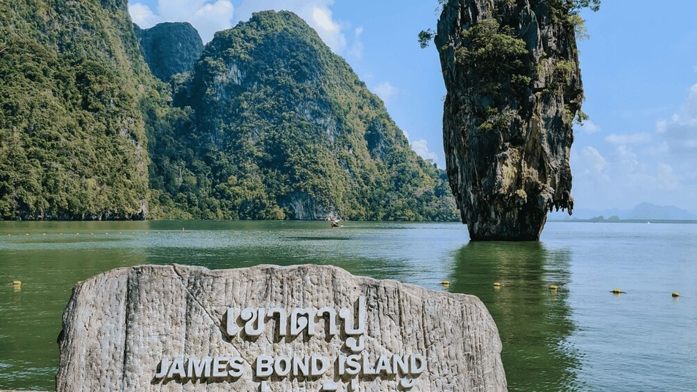 A stone sign with 'James Bond Island' inscribed, surrounded by a body of water and lush green mountains. 2