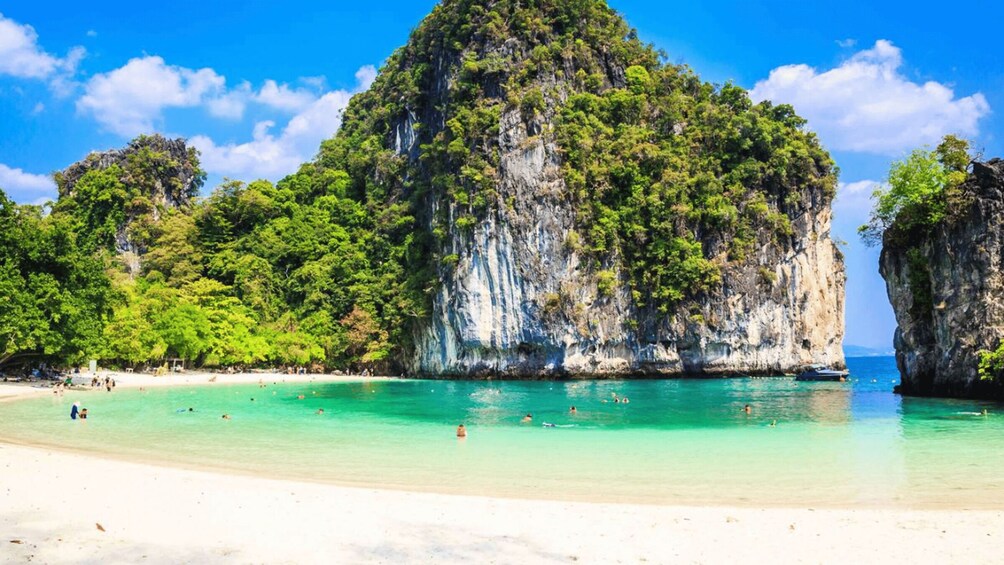 A beach with clear turquoise water, people swimming, and lush green cliffs. 5