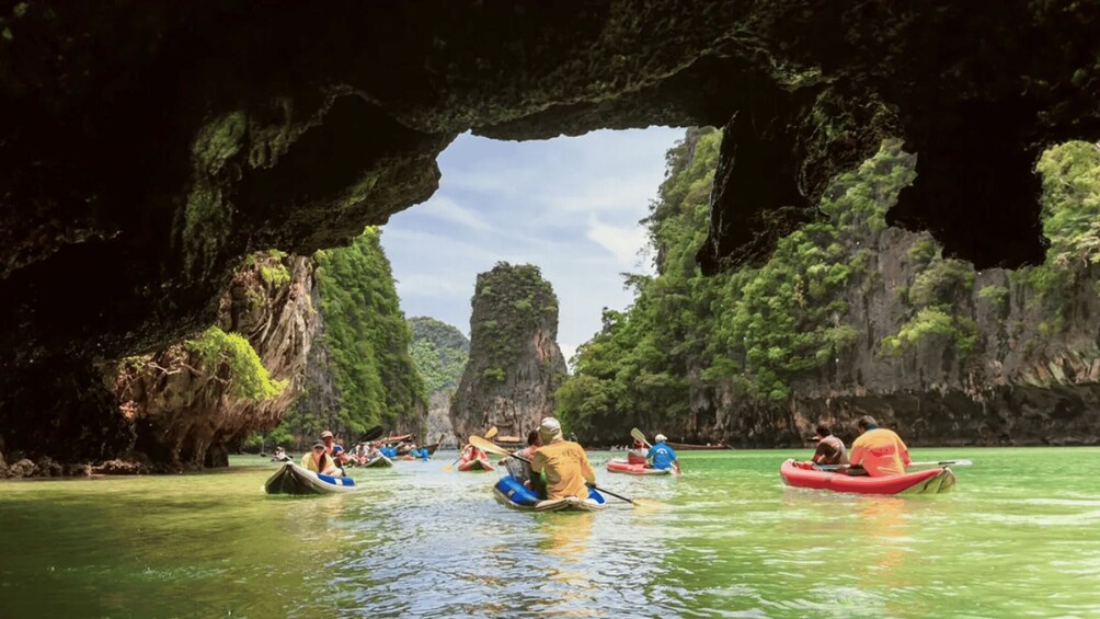 People kayaking in a river with a large cave opening in the background. 4