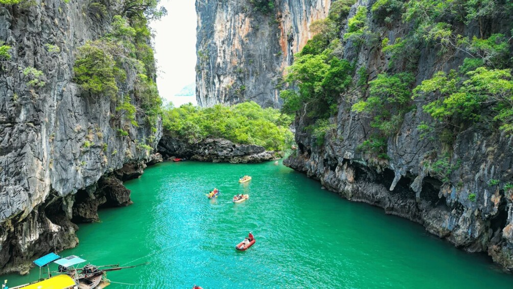 A narrow canyon with clear turquoise water, surrounded by steep cliffs and lush greenery. 1