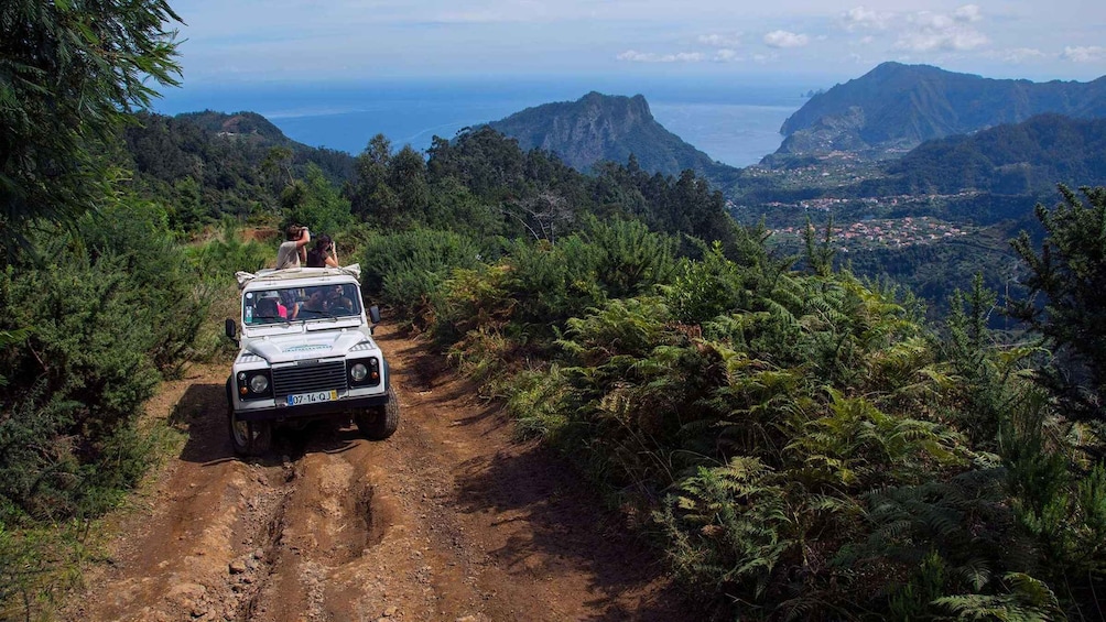 A white off-road vehicle on a dirt path surrounded by dense forest and mountains. 1