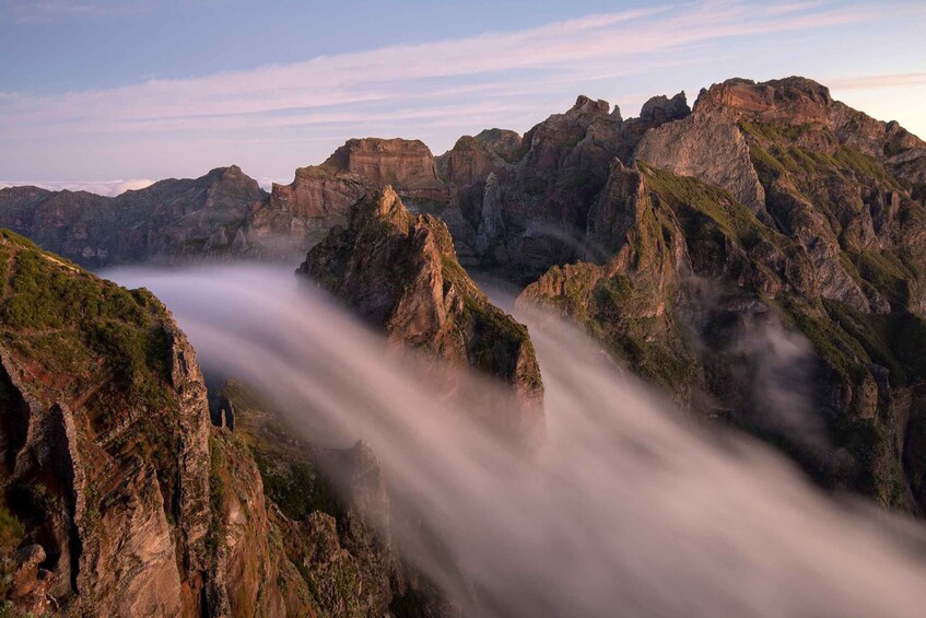 A mountainous landscape with rugged cliffs and a valley shrouded in mist. 2