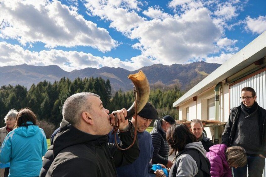 Un grupo de personas al aire libre, algunas sosteniendo un objeto similar a un cuerno, con montañas al fondo. 5