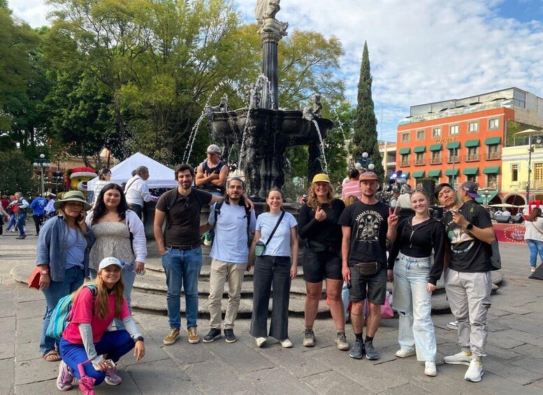 A group of people posing in front of a fountain with a statue, surrounded by trees and buildings. 1
