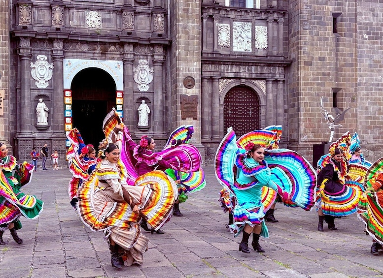 A group of dancers in colorful traditional attire performing in front of a historic building. 4