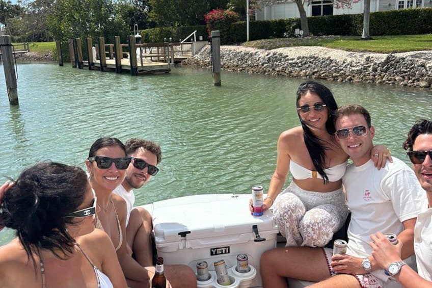 A group of people on a boat near a dock with a body of water and greenery in the background. 5