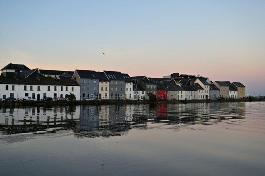 A waterfront with multi-story buildings reflecting on calm water during sunset. 5