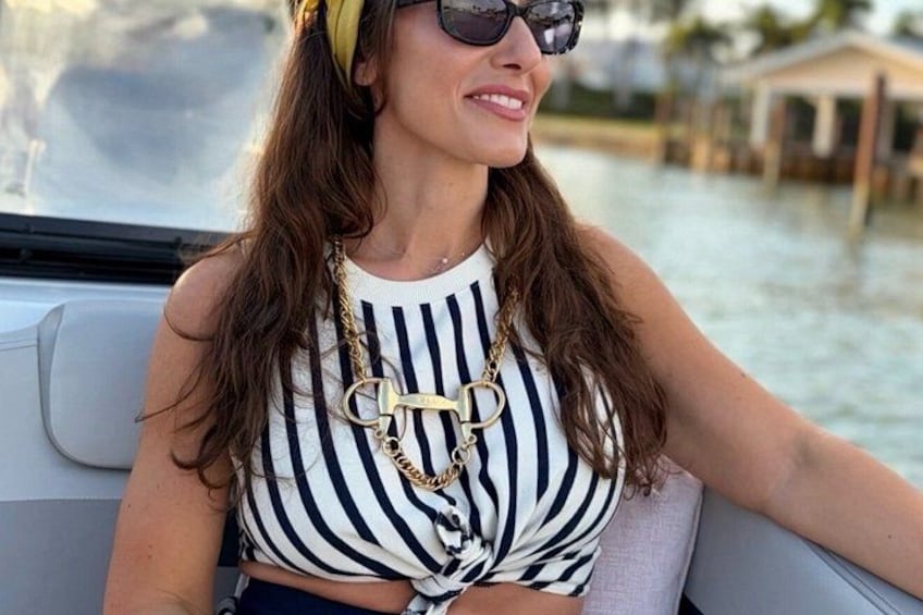 Una persona con remera a rayas y un collar dorado, sentada en un bote con agua y edificios al fondo. 2