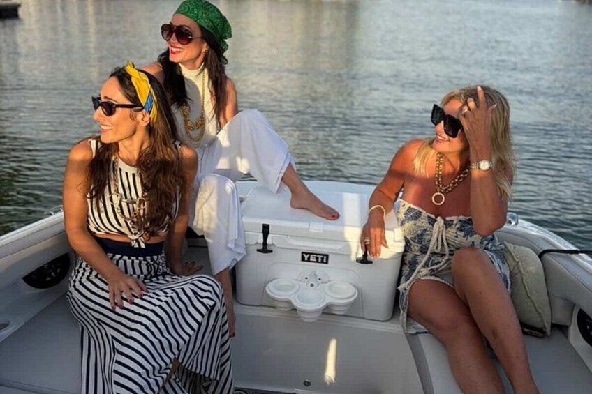 Three people on a boat with a cooler labeled 'YETI' and a water body in the background. 4