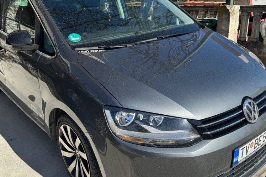 En grå Volkswagenbil med ett blått registreringsnummer, parkerad på en gata. 3