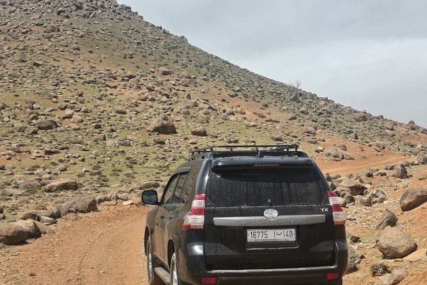En svart SUV kör på en stenig grusväg, och registreringsskylten visar numret 16775. 4