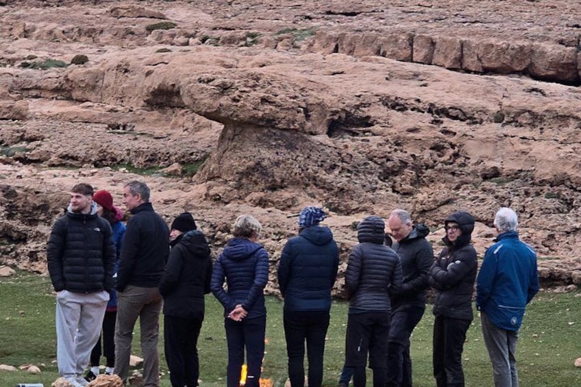 En grupp människor som står utomhus, troligen på en stenig mark med gles vegetation. 2