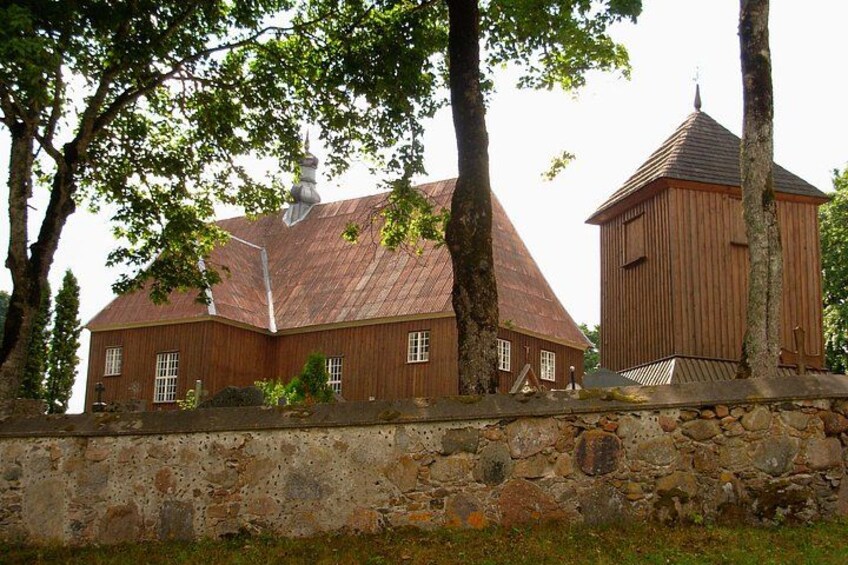 Una iglesia de madera con techo rojo y un muro de piedra en primer plano. 3