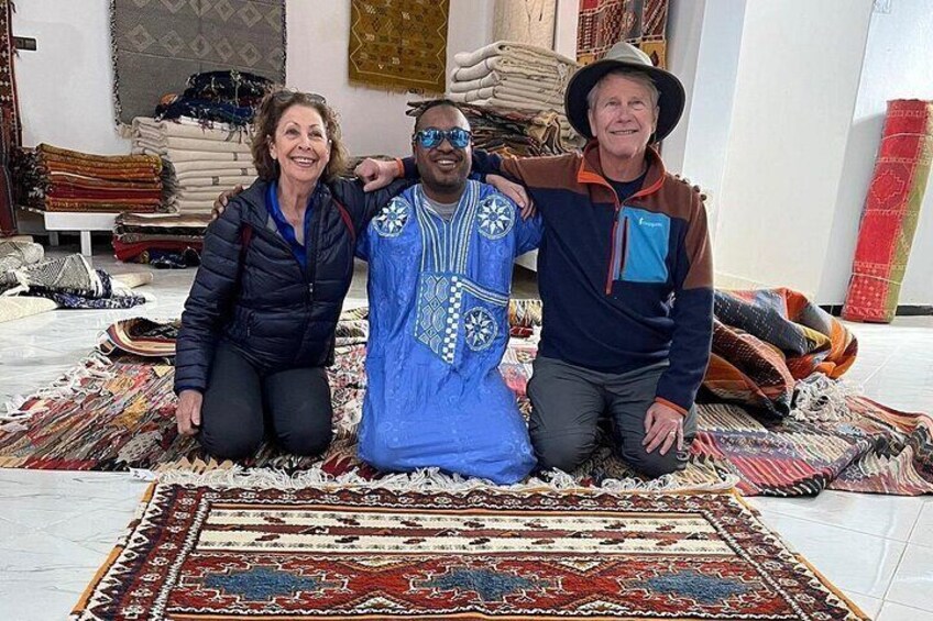 Three people posing with a large, patterned rug in a room filled with various textiles. 4