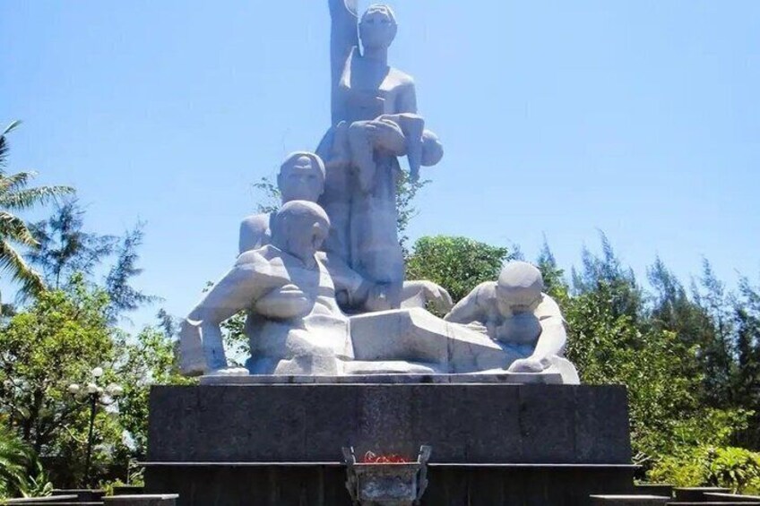 A stone monument with figures in various poses, surrounded by greenery. 5