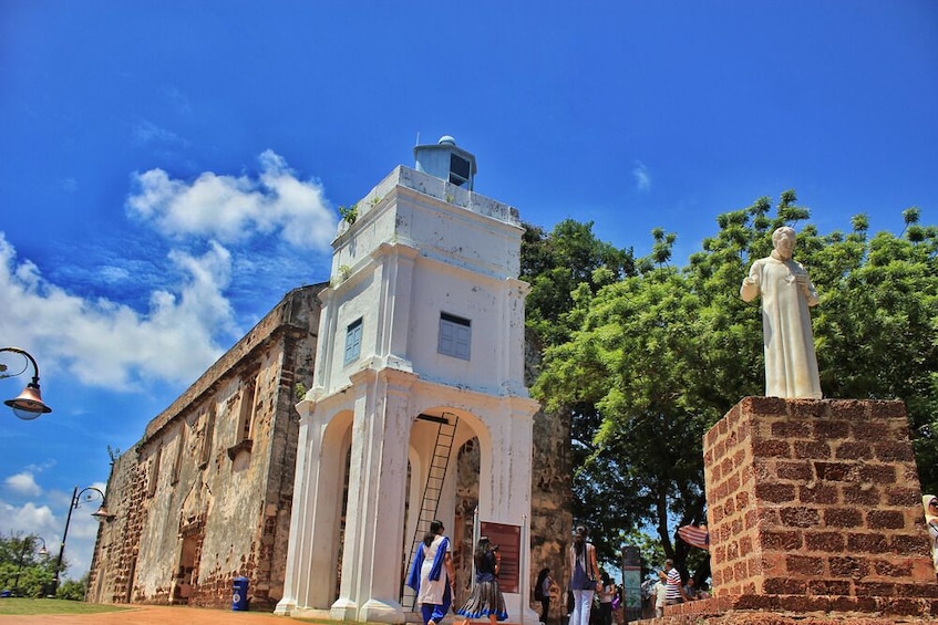 An old church with a bell tower, a statue, and people around. 5