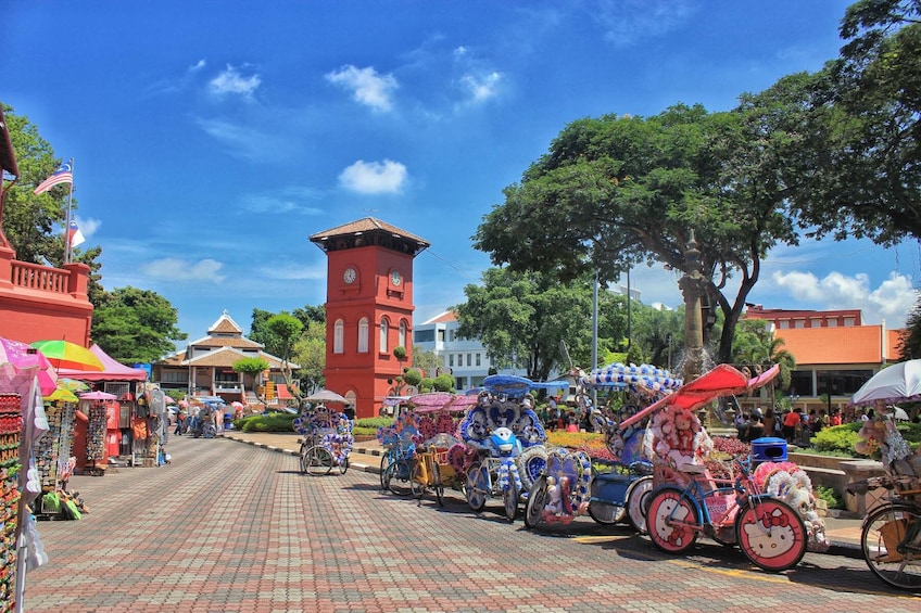 A vibrant street market with colorful stalls, a red clock tower, and decorated bicycles. 1