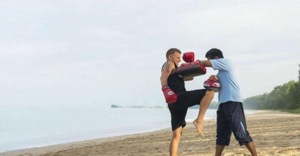 Two people practicing martial arts on a beach with a body of water and trees in the background. 1