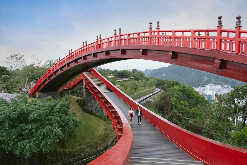 A red bridge with a curved design, surrounded by lush greenery and hills in the background. 3