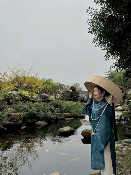 A person in traditional attire standing by a pond with koi fish, surrounded by rocks and greenery. 4