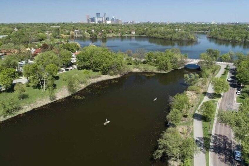 A river with a swan, surrounded by greenery and a city skyline in the distance. 1