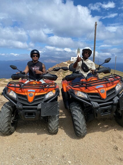Two people on orange ATVs with a lighthouse in the background. 2