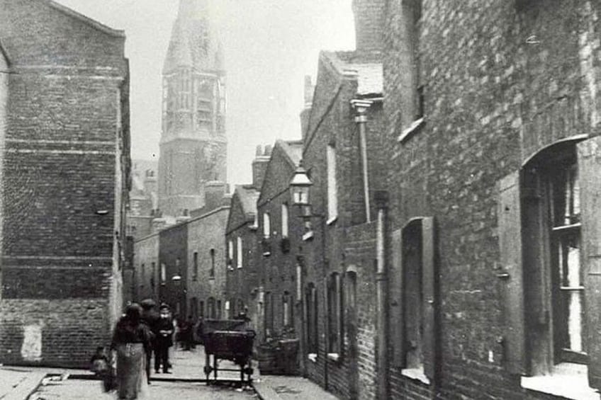 Une rue étroite bordée d’immeubles en briques, un chariot tiré par un cheval et, au loin, le clocher imposant d’une église. 4