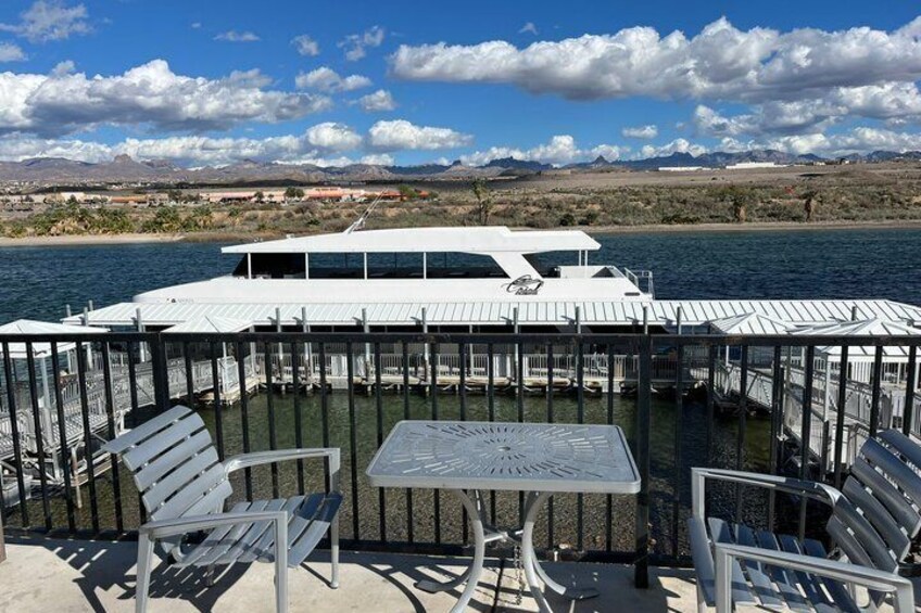 A docked boat with a white roof, surrounded by a metal railing, and a table with chairs in the foreground. 5