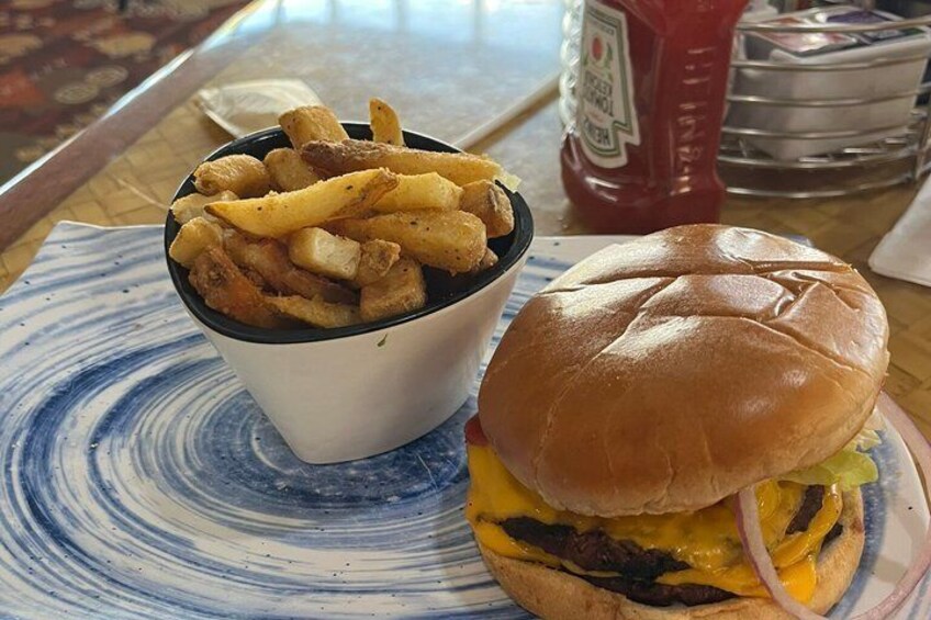 A burger with cheese and onion, a side of fries, and condiments on a table. 4