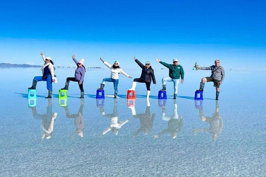 People standing on colorful blocks in a reflective salt flat under a clear sky. 2