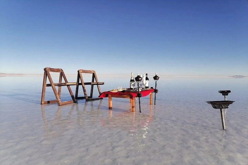 A salt flat with wooden chairs, a table, bottles, and a lamp. 3