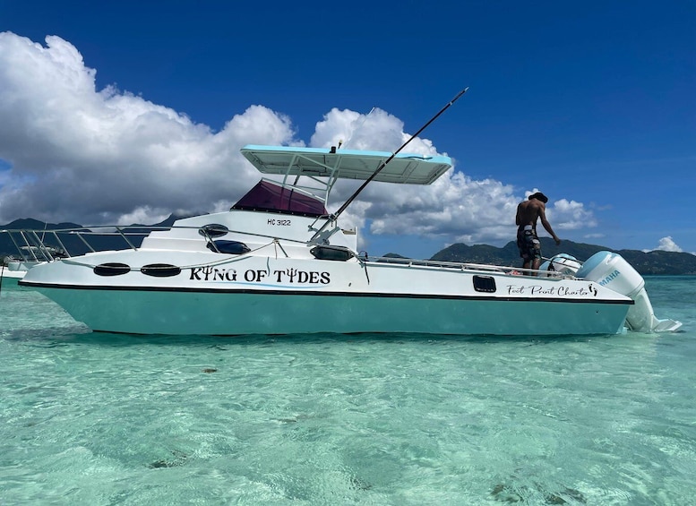 A boat named 'King of Tides' with a person on board, clear turquoise water, and mountains in the background. 5