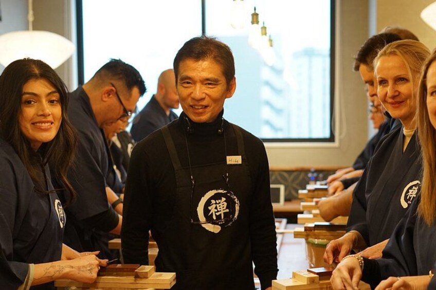 A group of people in a casual setting, some wearing dark clothing with a logo, and wooden blocks on a table. 2