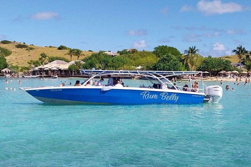 A blue boat named 'Rum Belly' on clear turquoise water with a beach and palm trees in the background. 5