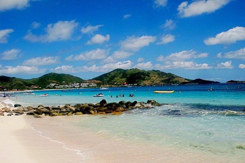 A beach with clear turquoise water, rocky shoreline, and distant hills. 4