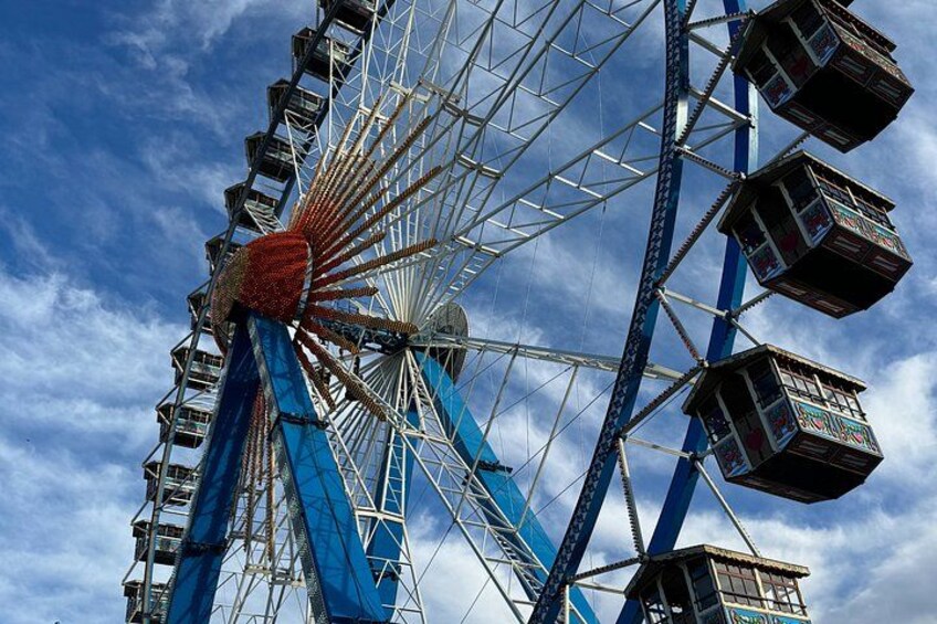 Ein großes Riesenrad mit blauen und weißen Gondeln vor einem teils bewölkten Himmel. 3