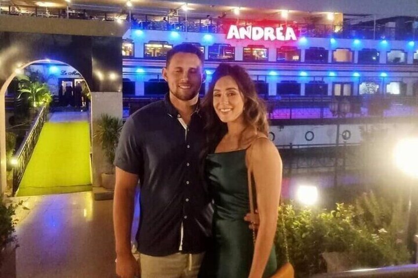 A couple standing in front of a brightly lit restaurant named 'ANDREA' with outdoor seating. 4