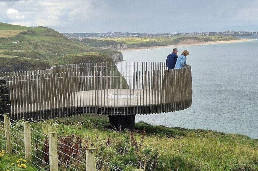 A curved wooden bench overlooking a coastal landscape with hills and a beach. 3