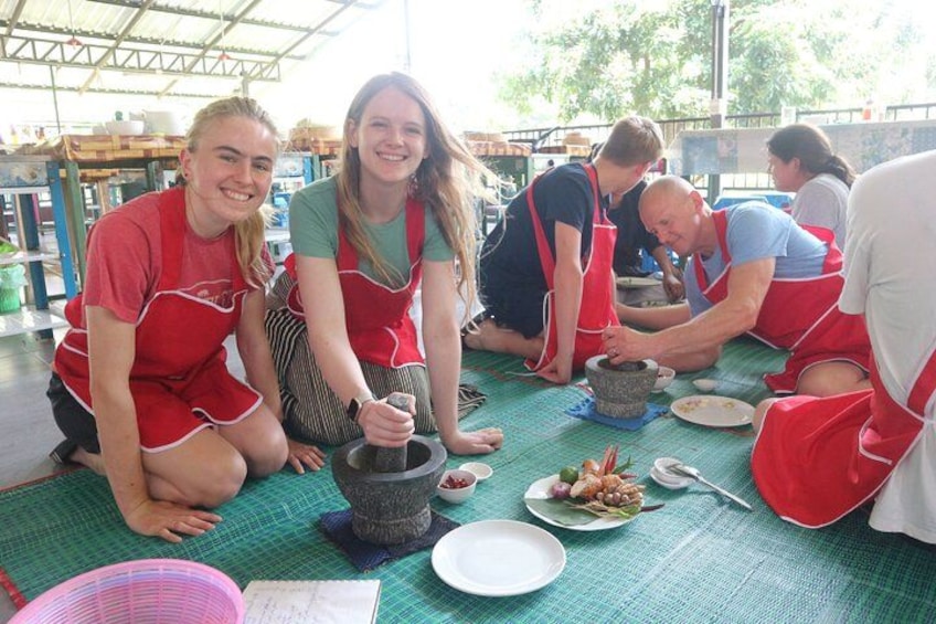 People in aprons grinding ingredients on a mat. 3