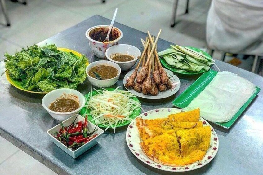 A table with various dishes including a plate of yellow curry, fresh vegetables, and skewered meat. 5