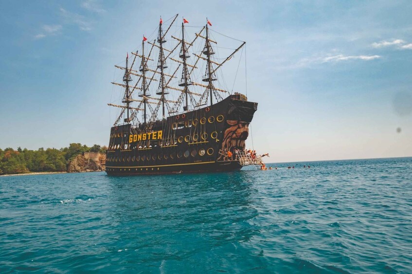 A tall ship named 'GODSTRENG' sailing on the sea with a rocky coastline in the background. 4
